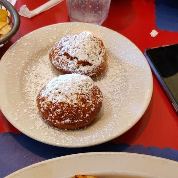 Two powdered sugar-dusted beignets on a white plate, with tortilla chips and a phone nearby.